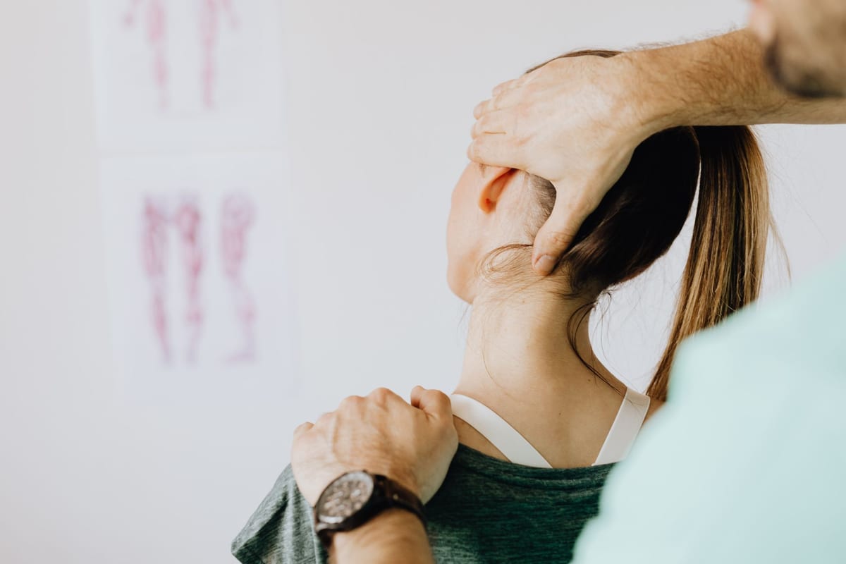 A clinician guiding a gentle neck stretch in front of anatomy charts