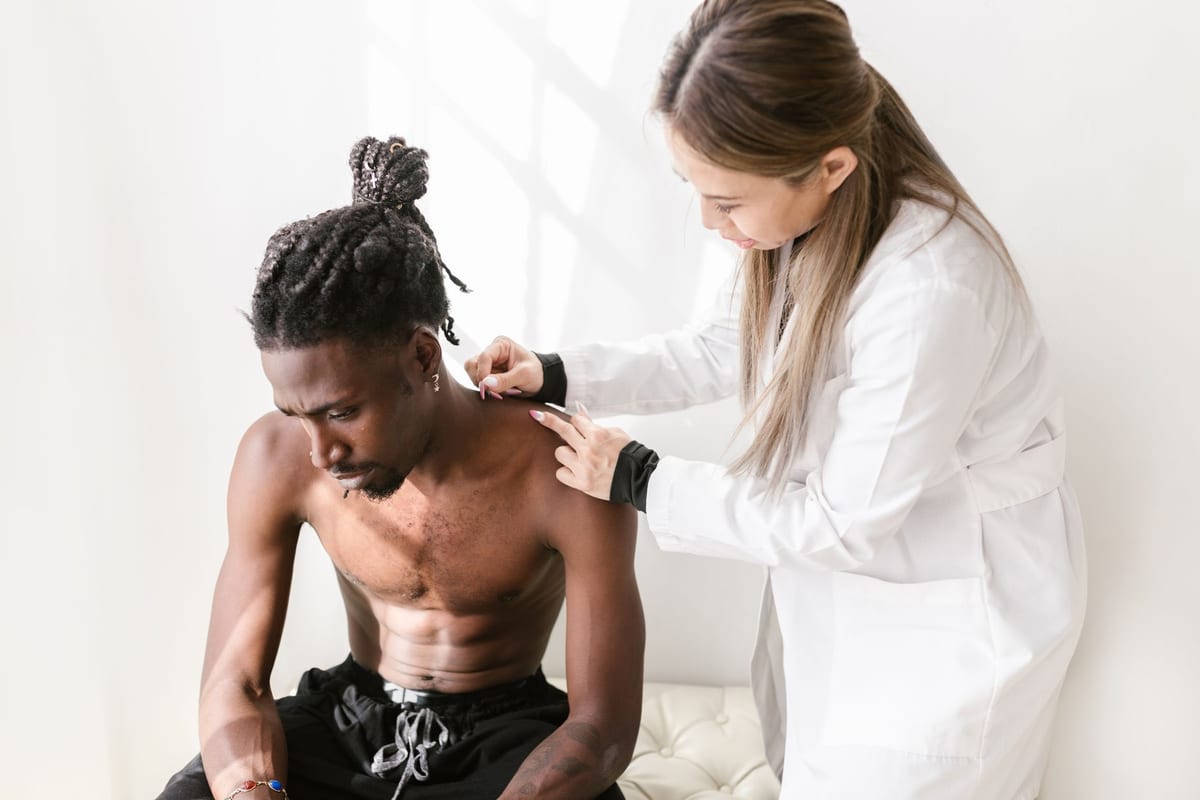A practitioner placing fine needles at a patient's shoulder